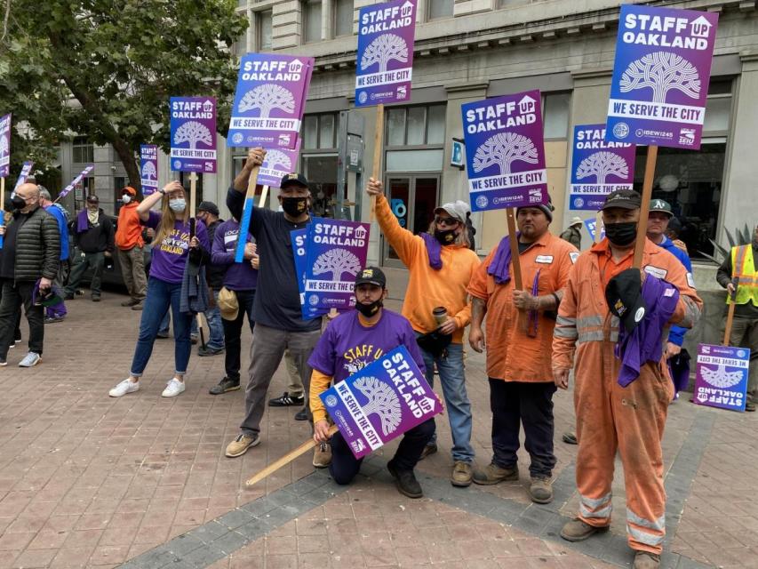Worker stand outdoors holding "Staff Up City of Oakland" signs at a picket