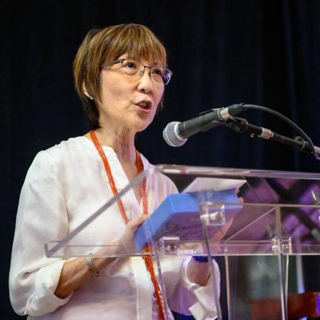 Wilma Chan speaking behind a clear lucite podium.