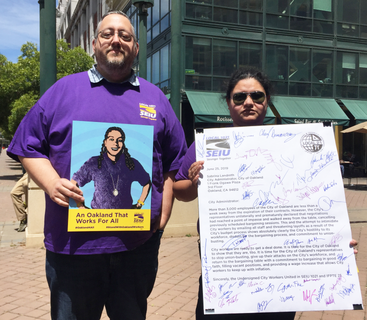 Two proud City of Oakland workers hold an SEIU 1021 poster and the letter our members delivered to Sabrina Landreth.