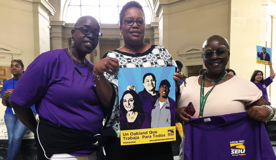 Three proud City of Oakland workers show their SEIU 1021 shirts and a poster.