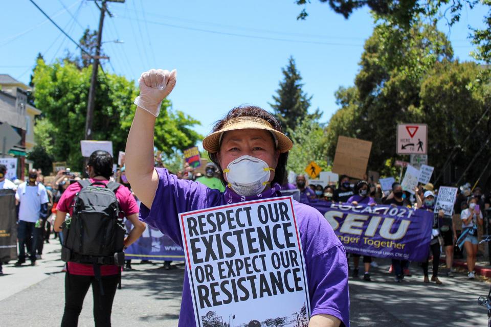 Yeon Park, SEIU Local 1021's East Bay Region Vice President Holds a Sign Reading "RESPECT OUR EXISTENCE OR EXPECT OUR RESISTANCE" in  front of a group of striking workers during the Alameda Health System strike.