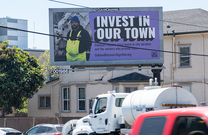 A billboard featuring an SEIU 1021 member, reading "Invest in our town. Oakland's leaders must invest in city services and the workers who provide them."