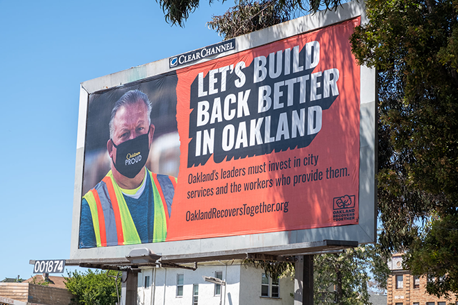 A billboard featuring a City of Oakland worker, reading "Let's Build Back Better in Oakland"